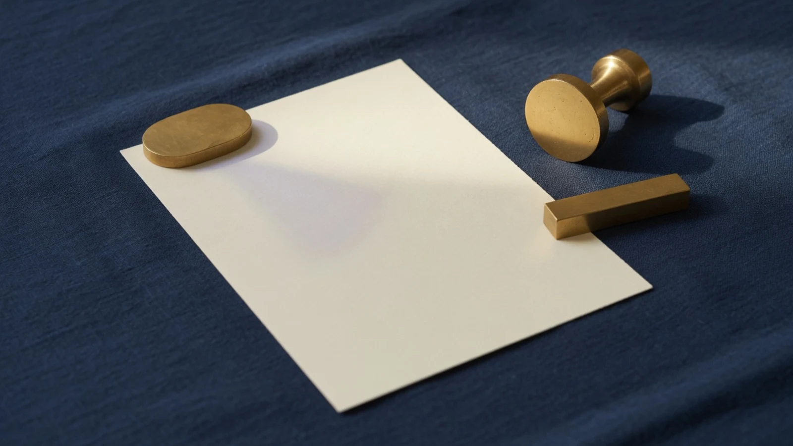 A blank cream card under a brass weight, with an unused stamp set aside on navy cloth