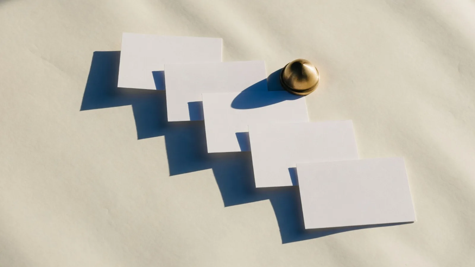 Blank index cards in a loose line with a brass weight on cream paper